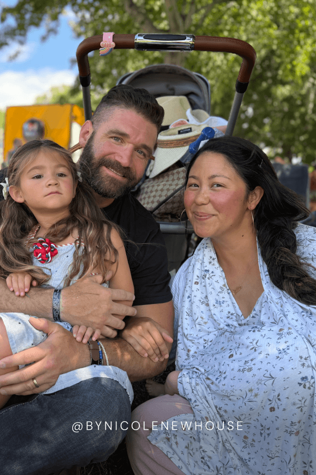 Family of three with a stroller in an outdoor setting while mom covers baby with birthday botanical nursing cover. Text reads @NICOLENEWHOUSE