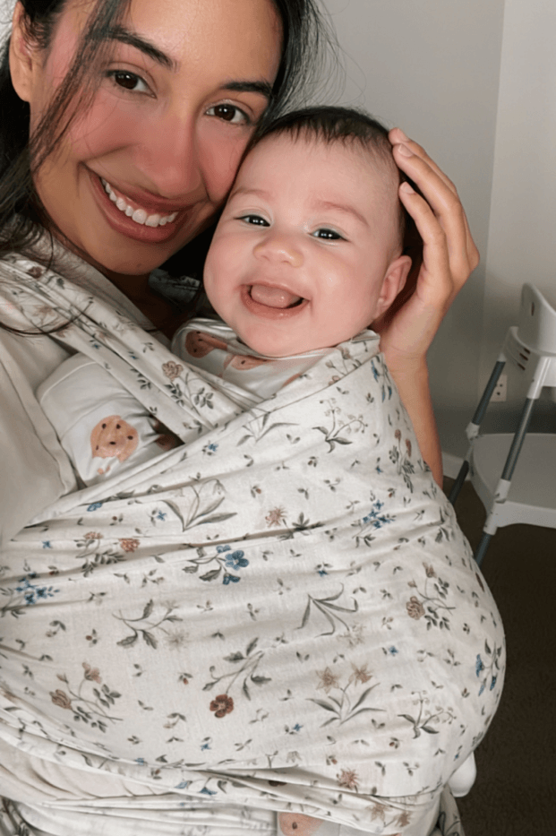 Woman smiling with a baby wrapped in a floral-patterned wrap.