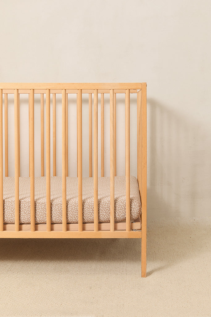 A simple wood crib styled with a Solly Baby Crib Sheet in the Cream Floral print featuring petite cream buds gently scattered atop a soft taupe brown base.