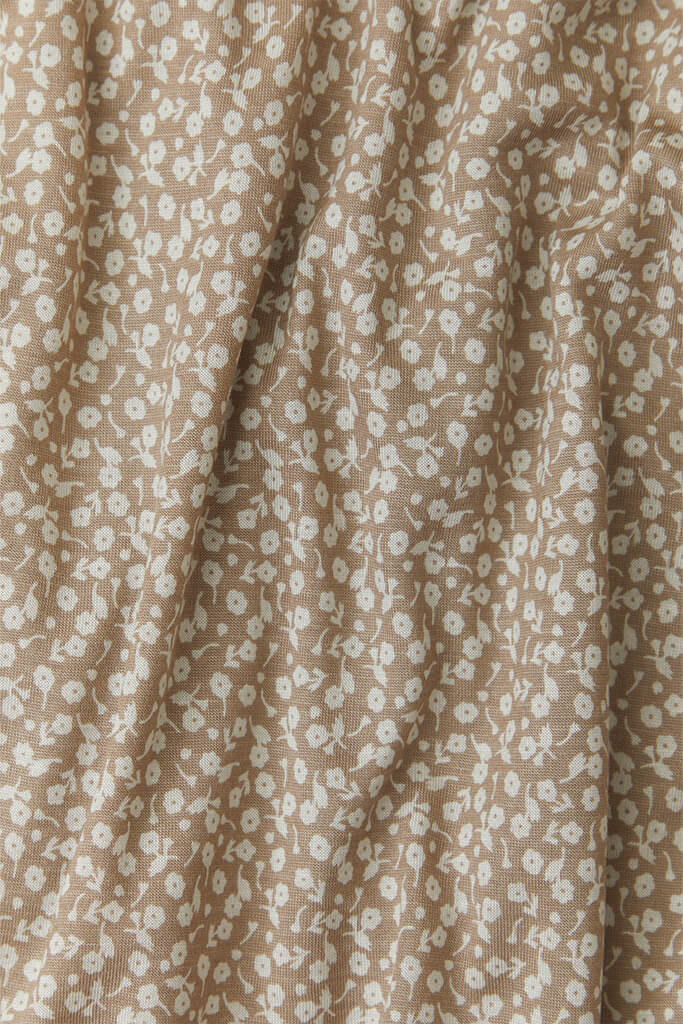 A close-up fabric shot of Solly Baby's Cream Floral print, featuring petite cream buds gently scattered atop a soft taupe brown base.