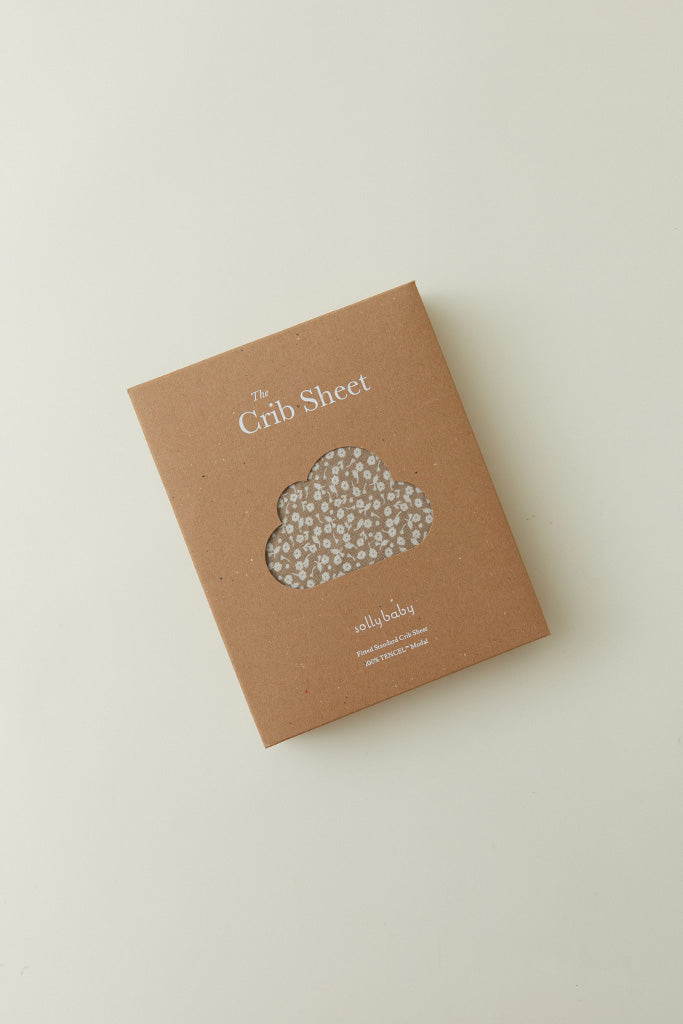 A product packaging shot of the Solly Baby Crib Sheet in a brown box with a window showing the Cream Floral print inside. 