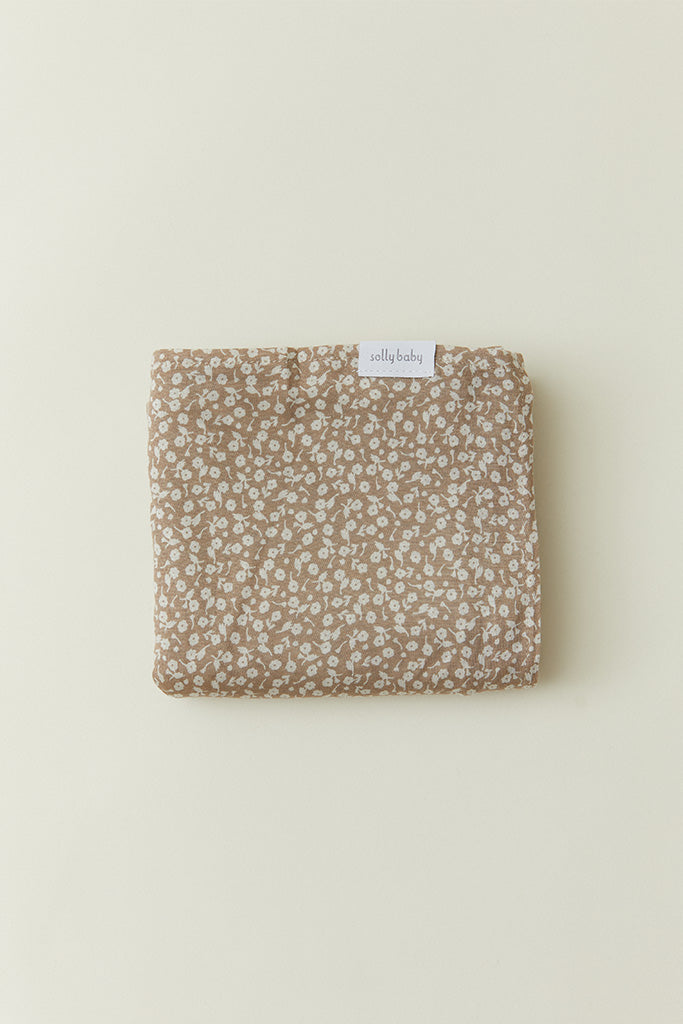 A neatly folded Solly Baby swaddle in the Cream Floral print, showcasing petite cream buds gently scattered atop a soft taupe brown base. The Solly Baby tag is visible at the top center.