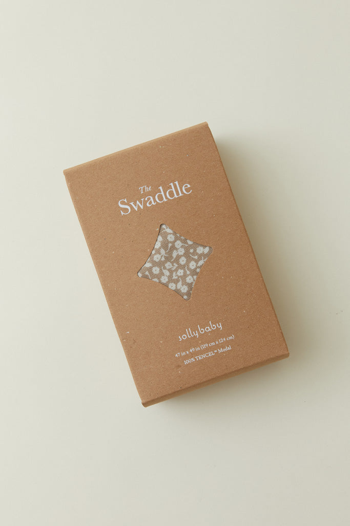 A product packaging shot of the Solly Baby Swaddle in a box with a window showing the Cream Floral print inside. 