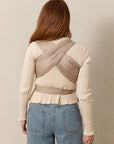The back view of a woman wearing a Solly Baby Wrap carrier in the Cream Floral print, featuring delicate cream flowers on a taupe background, tied securely at her waist over a cream sweater and jeans.