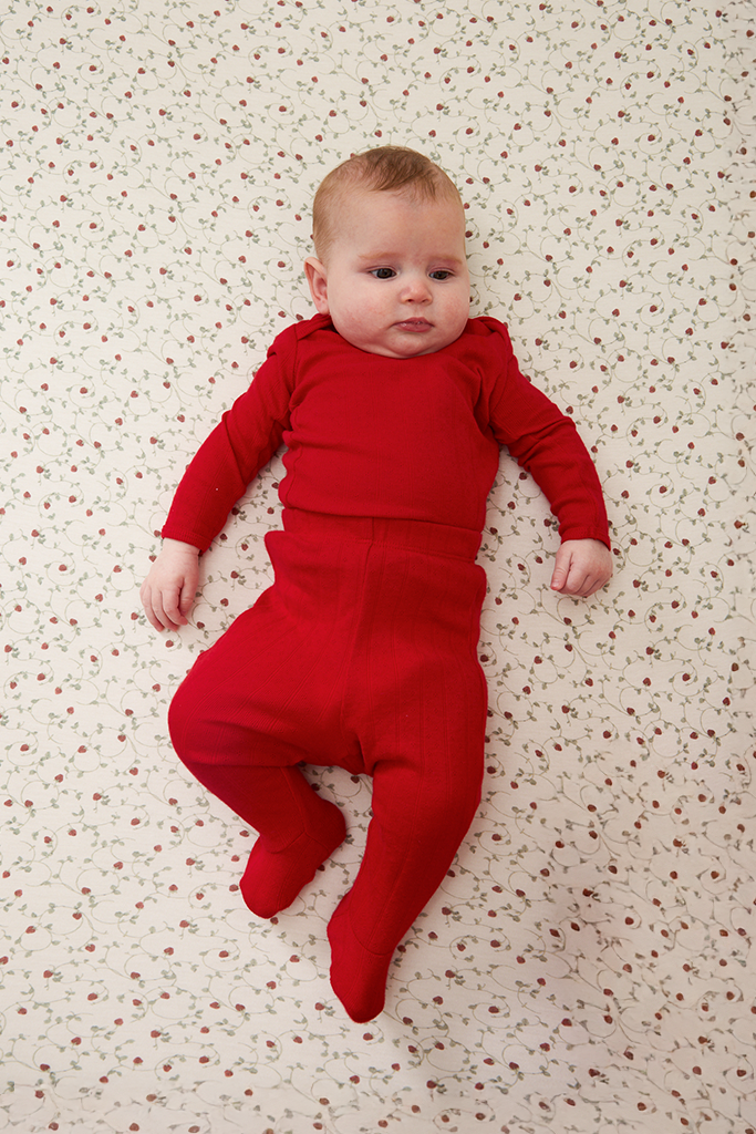 Baby wearing a red pointelle outfit lying on a strawberry patterned surface