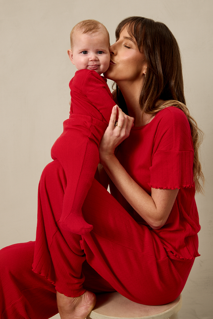 Woman in a red pointelle outfit holding a baby in red pointelle outfit against a beige background