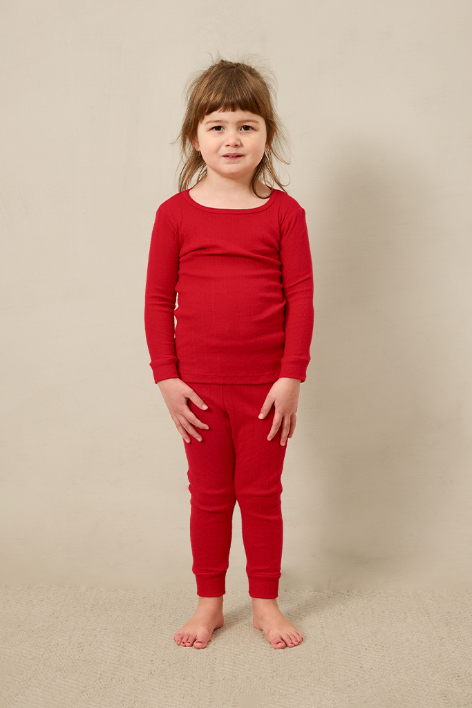 Young girl wearing a red pointelle outfit against a beige background