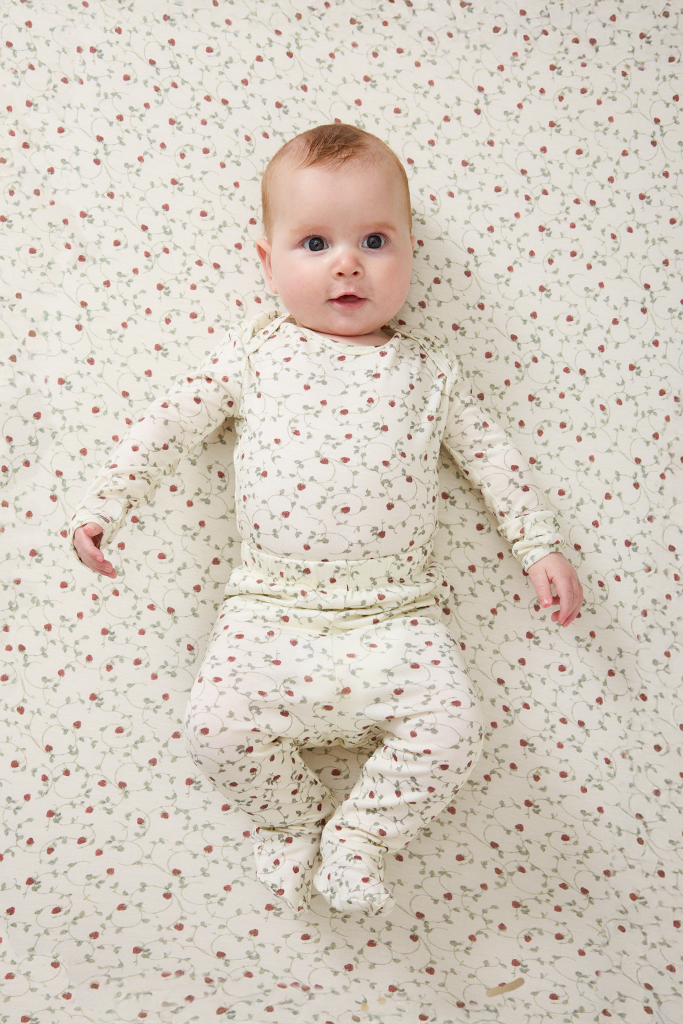 Baby in a strawberry outfit lying on a matching patterned blanket