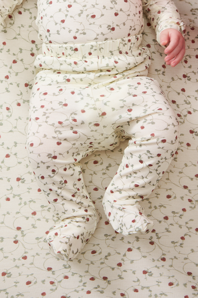 Baby in a strawberry outfit with red strawberries lying on a strawberry-patterned blanket