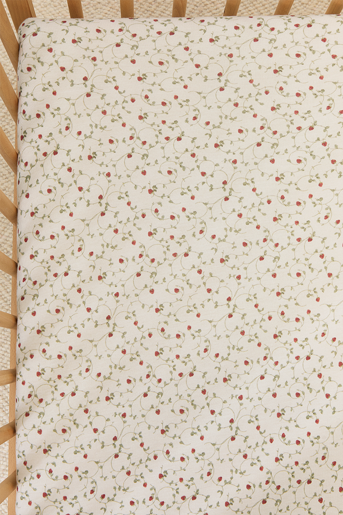 Top view of a crib sheet with a dainty hand-painted strawberry vine print.