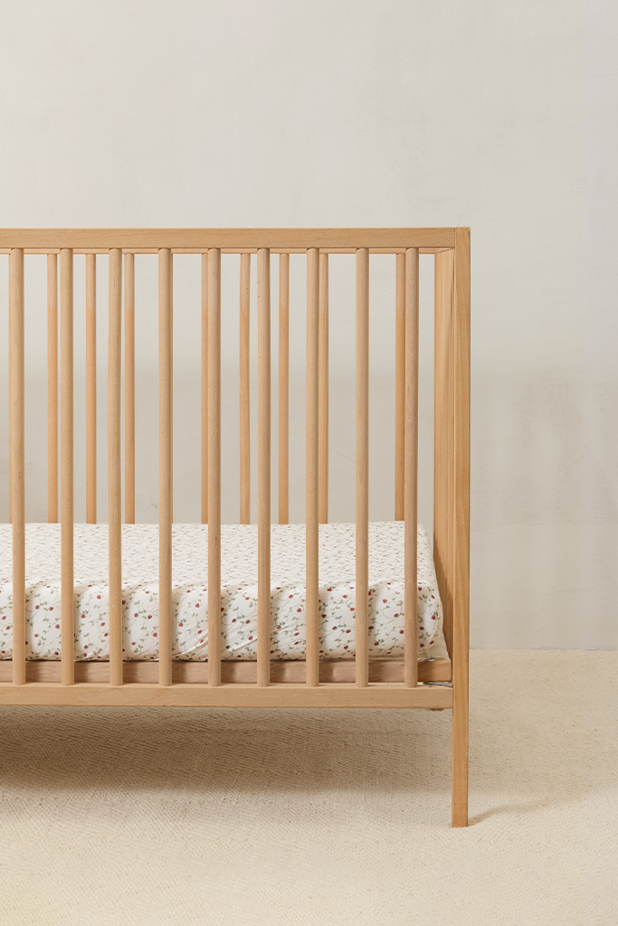 Wooden crib with crib sheet in strawberry print, featuring a delicate hand-painted strawberry vine on a soft neutral background.