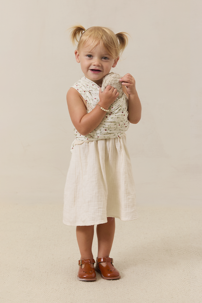 Young girl in a white dress wearing a strawberry solly dolly carrying a stuffy on beige background