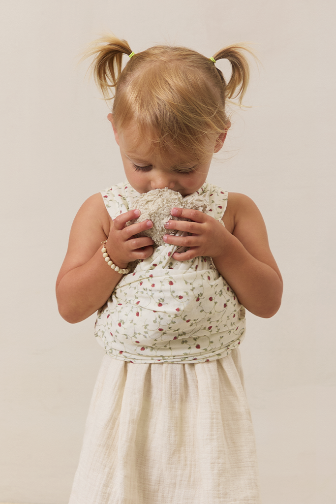Young girl in a white dress wearing a strawberry solly dolly carrying a stuffy on beige background