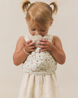 Young girl in a white dress wearing a strawberry solly dolly carrying a stuffy on beige background