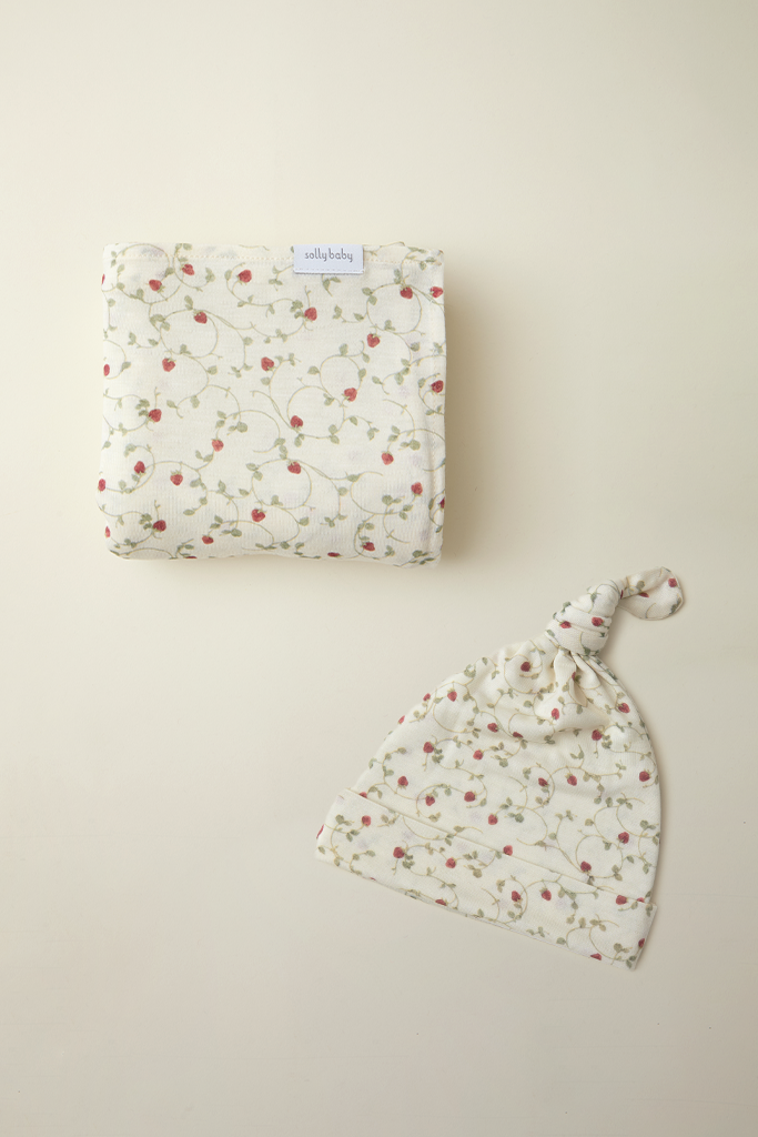 Strawberry-patterned baby blanket and hat set on a beige background