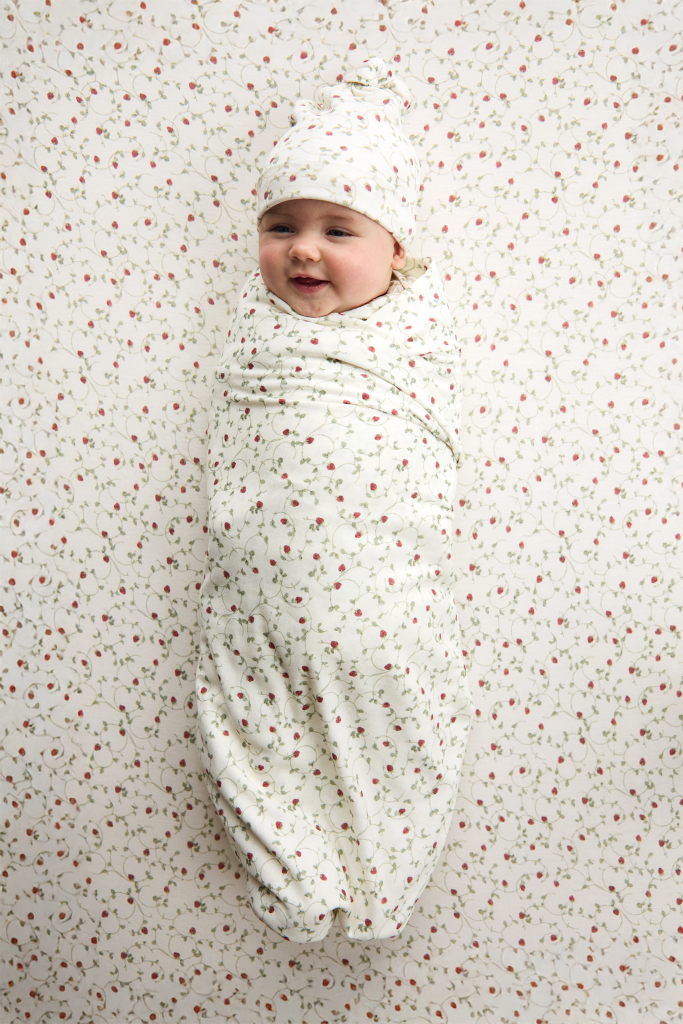Baby swaddled in a white blanket with red strawberry patterns on a matching background