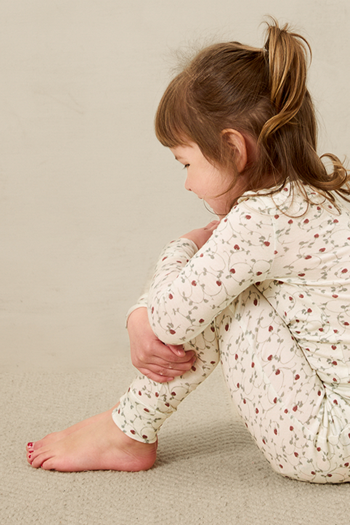 Child wearing a strawberry outfit sitting on a beige surface