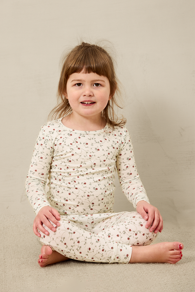 Young girl wearing a strawberry pajama set sitting on a beige floor.