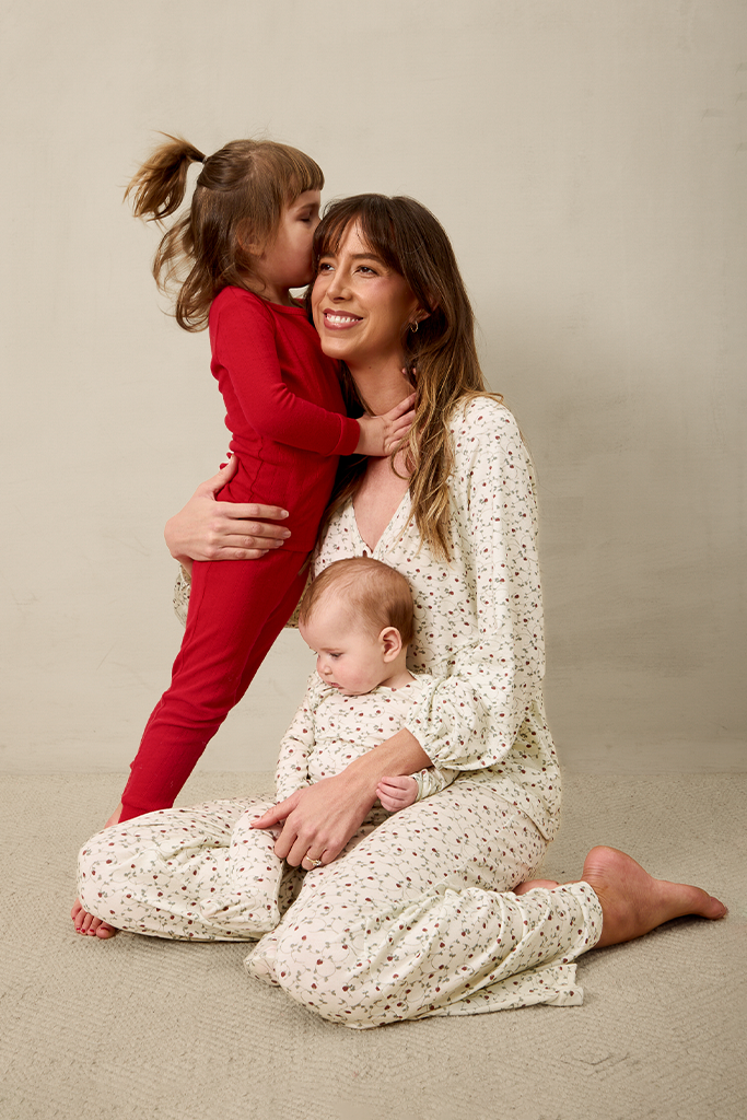 Woman in a white strawberry outfit sitting on the floor with two children, one in a red sleep outfit  and the other in a strawberry outfit.