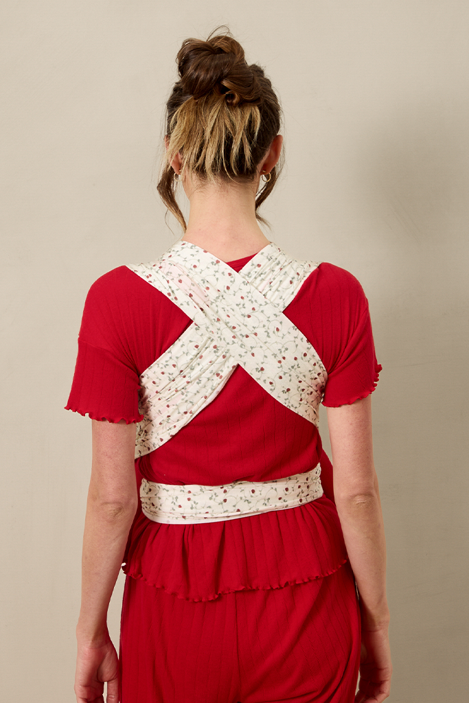 Person wearing a red outfit with a  strawberry baby wrap criss crossed in  the bag against a beige background