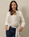 Woman holding a baby in a floral baby carrier against a plain background