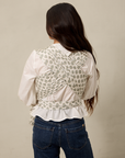 Woman wearing a white blouse with a patterned vest over a beige background