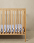 Wooden crib with blue and white patterned crib sheet on a mattress against a beige wall.