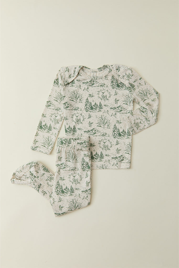 A flat lay of toddler pajamas in a cream and soft green winter forest toile design, available in sizes 12m-5T.