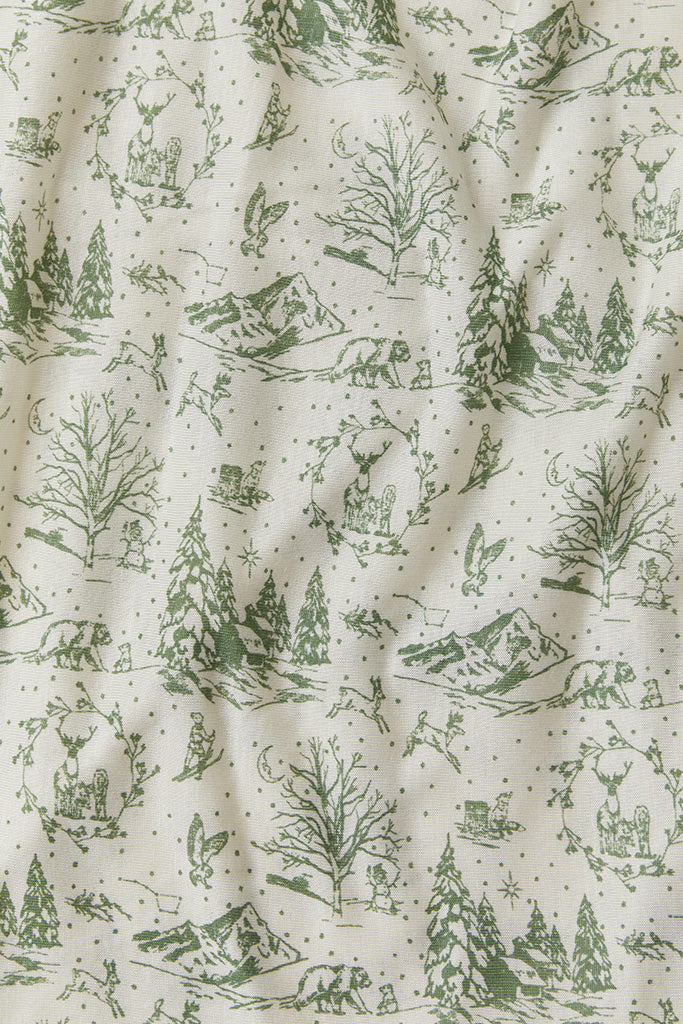 A close-up fabric shot of Solly Baby&#39;s Winter Toile print, featuring hand-drawn scenes of trees, animals, and mountains in a soft green on top of a cream background.