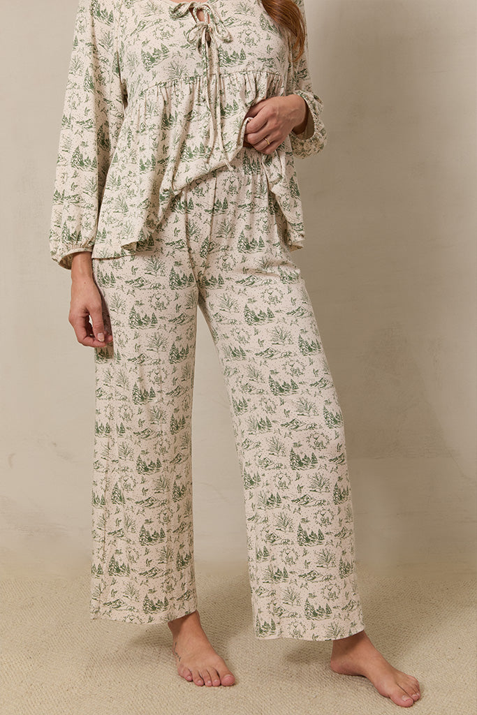 A close-up of a woman wearing wide-leg cropped pajama pants in a winter forest toile design, highlighting the comfortable, loose fit.